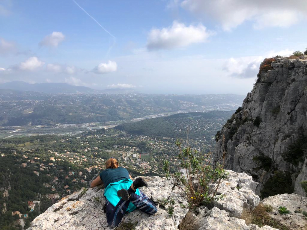 Personne allongée au bord d'une falaise, observant le paysage, symbolisant le lâcher-prise, l'acceptation, et l'accomplissement dans un moment de gratitude. Sophrologue Nice, inspirant le bien-être.