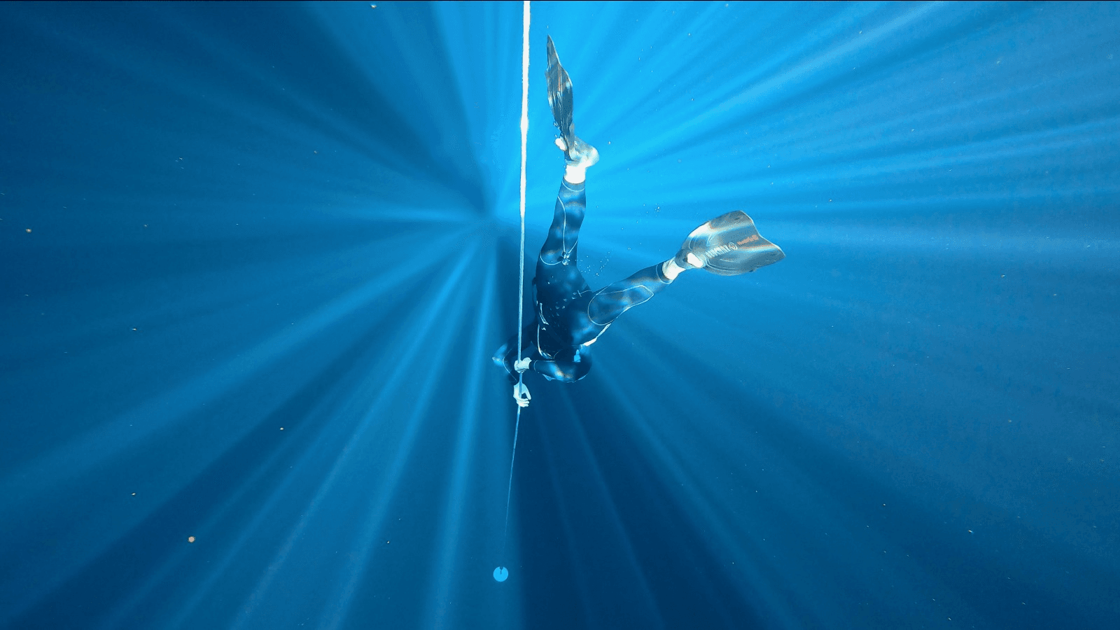 Apnéiste descendant en apnée verticale le long d'une corde, incarnant le lâcher-prise, la confiance en soi et la connexion corps-esprit dans l'immensité sous-marine.