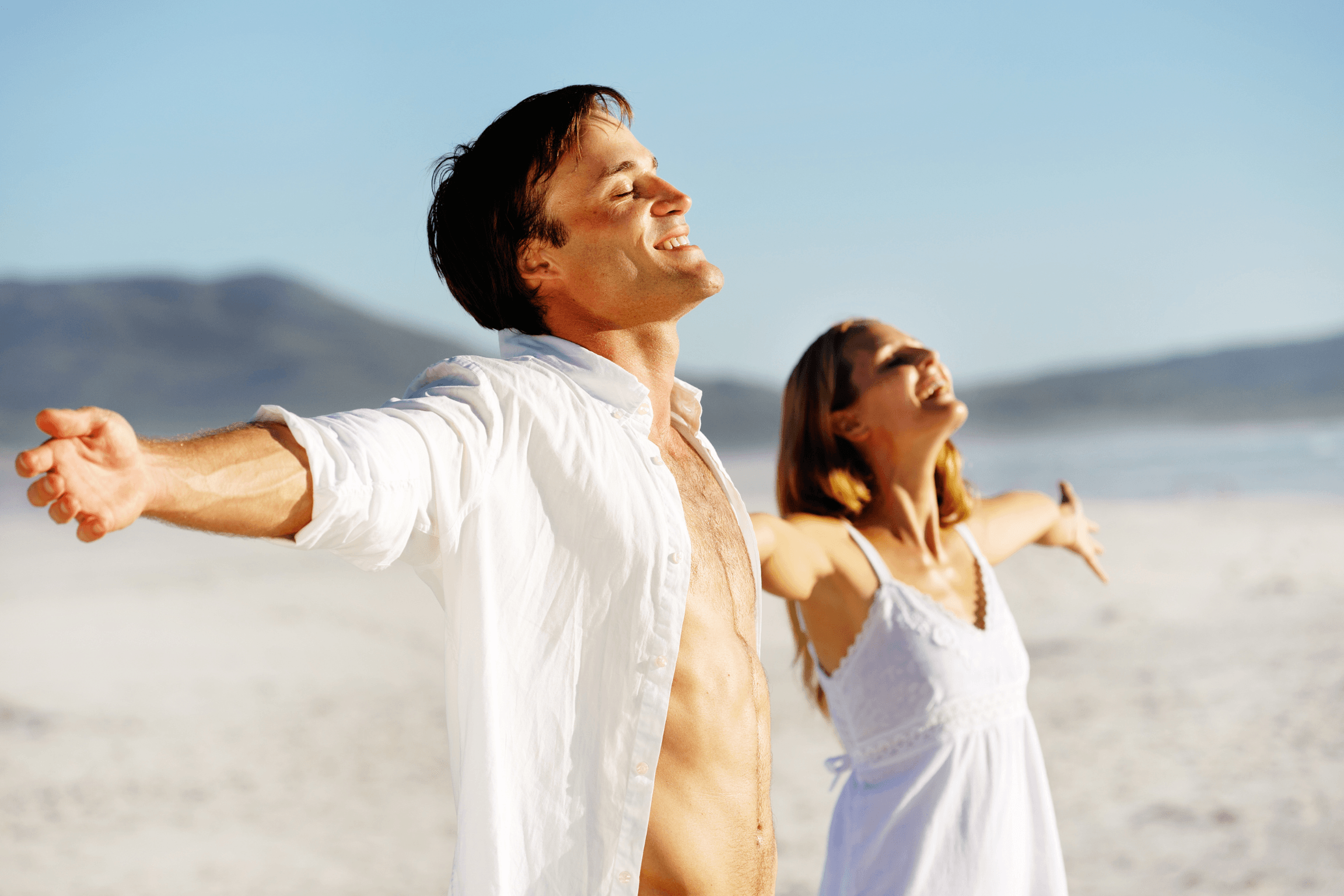 Un couple sur une plage en pleine respiration profonde, bras écartés vers le ciel, symbolisant l'épanouissement, le lâcher prise, et la connexion à soi, pouvant être obtenus par la sophrologie ou la respiration.