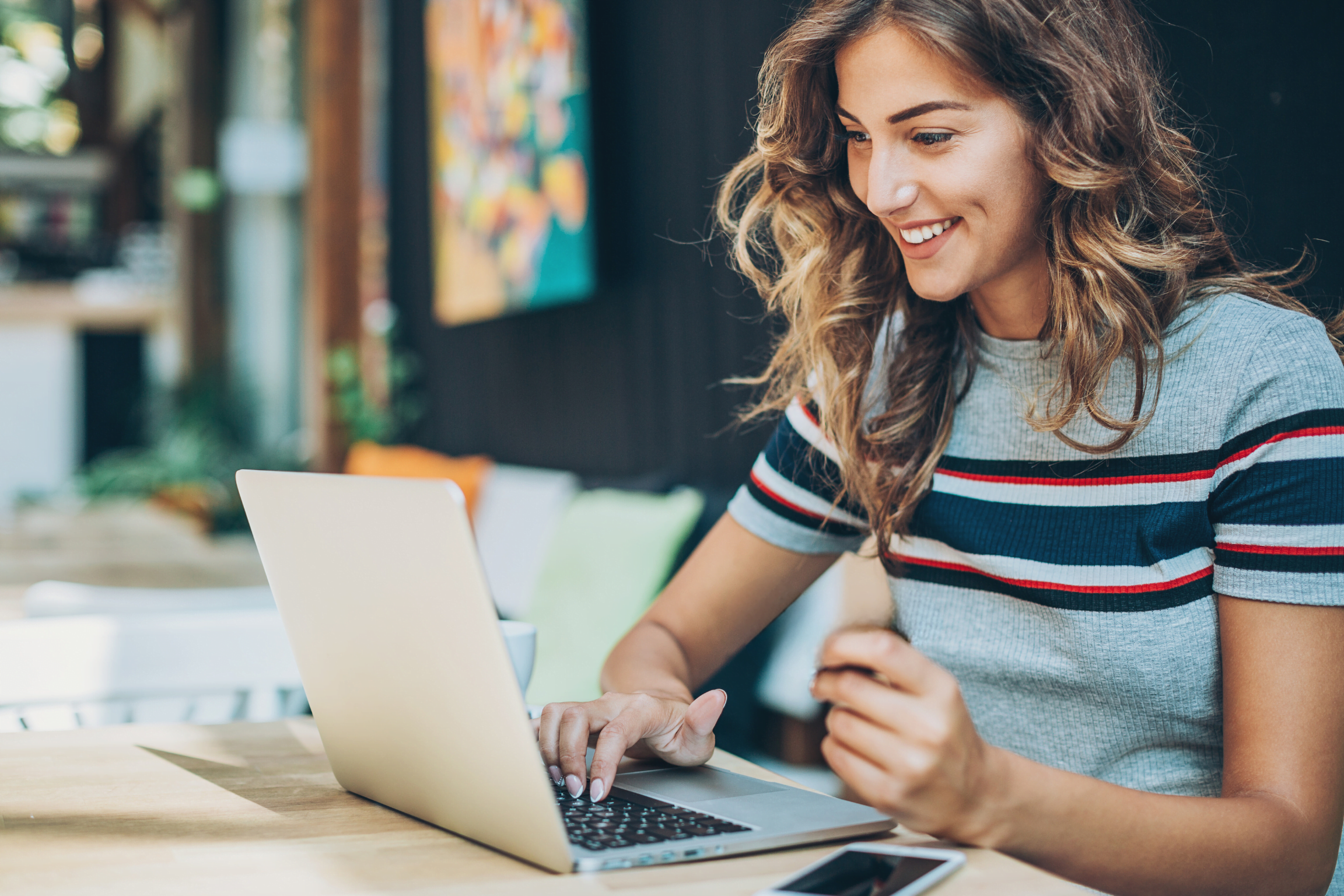 Femme souriante devant son ordinateur portable, en train de profiter des avanatges de faire une séance en ligne, en visio, représentant l'épanouissement, la flexibilité et le gain de temps.