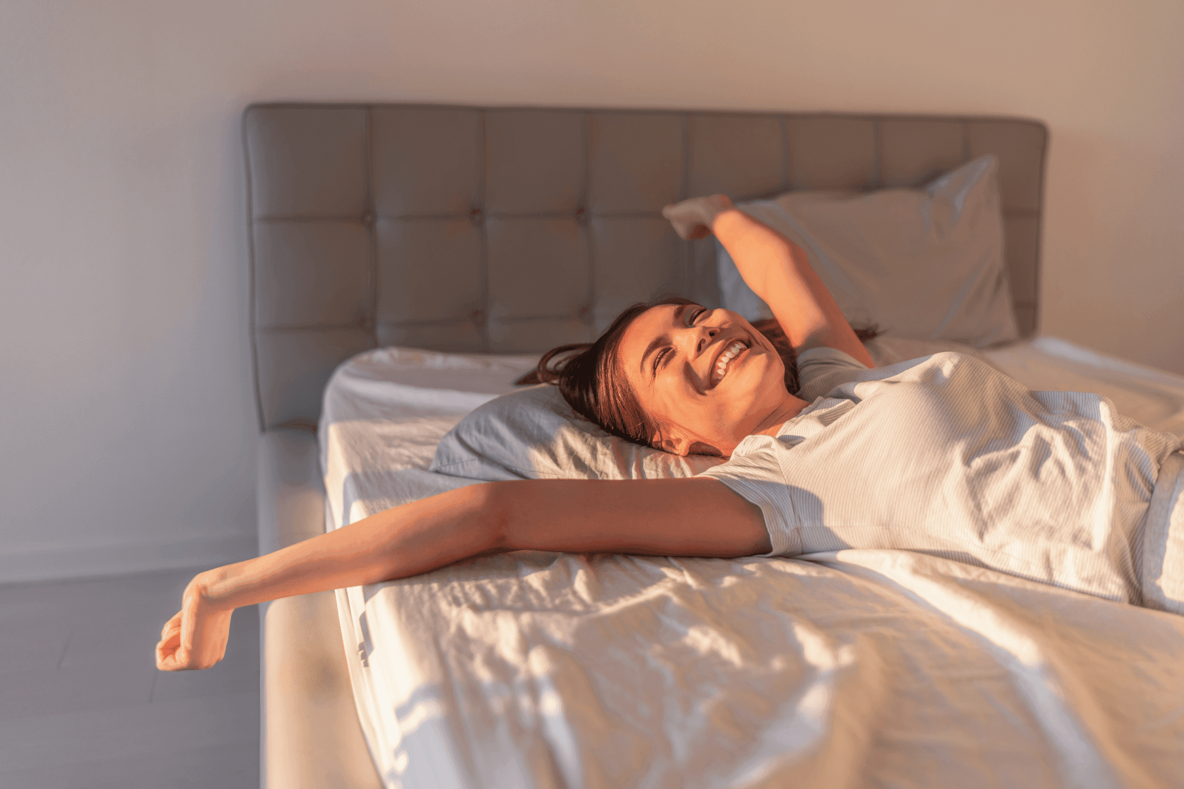 Femme souriante s'étirant dans son lit, représentant la qualité de sommeil et les bienfaits de la relaxation, avec des techniques comme la sophrologie ou la respiration.