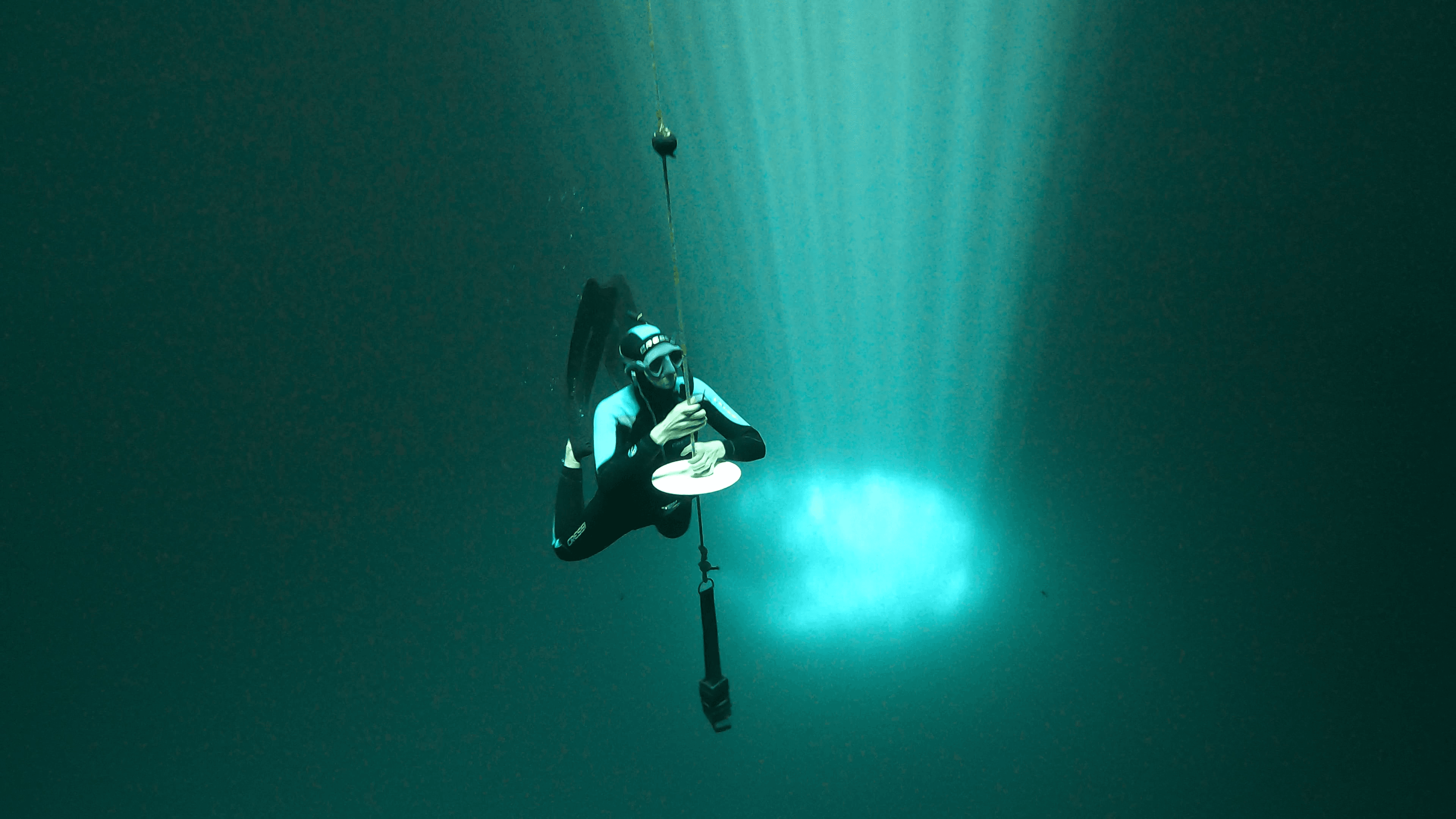 Femme en train de faire de l'apnée statique, relaxée, avec un puit de lumière dans l'eau, ce qui crée une atmosphère spirituelle