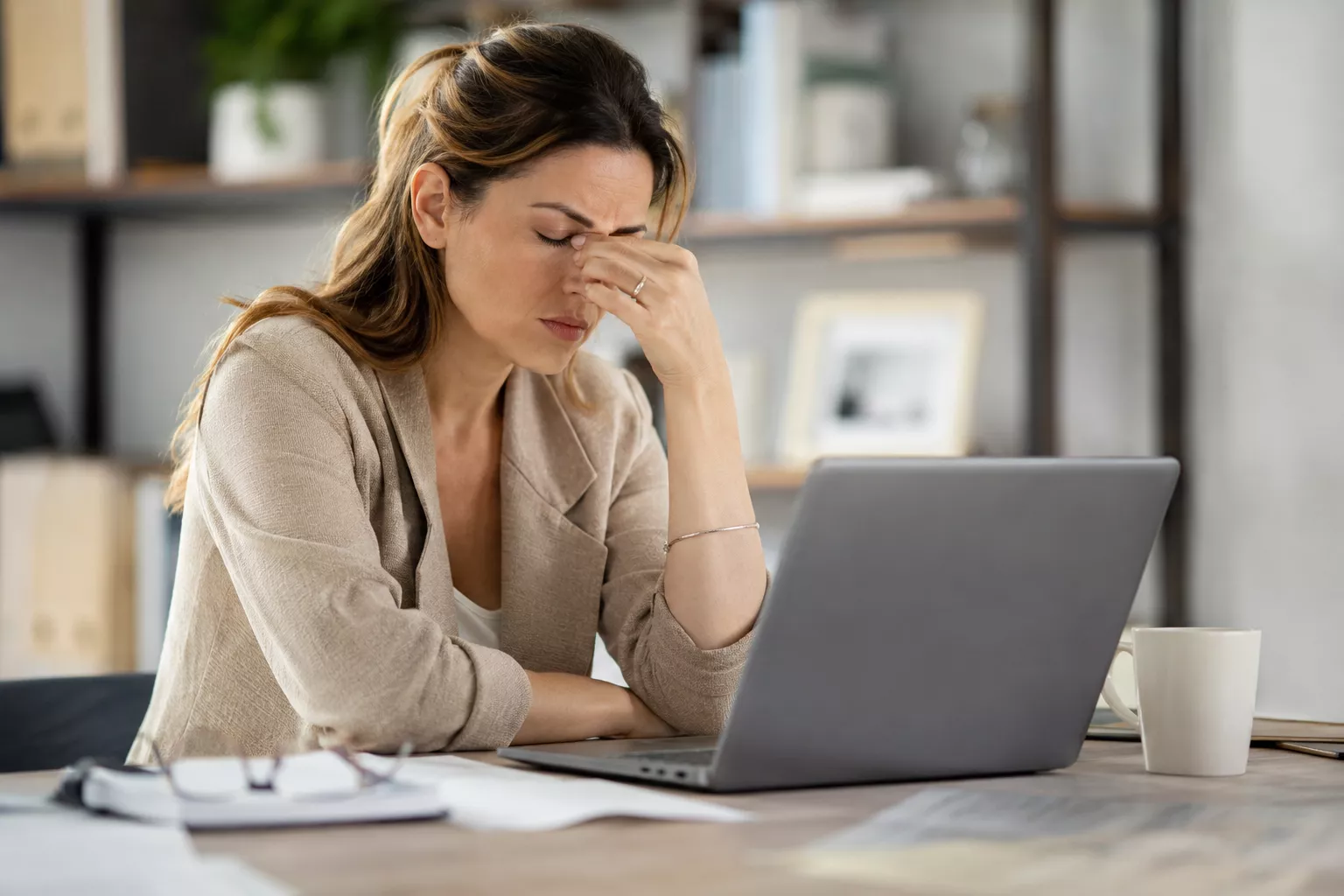 Femme en situation de surcharge mentale, assise à un bureau devant un ordinateur, le visage dans la main, exprimant du stress et de la fatigue mentale dans un environnement de travail moderne.